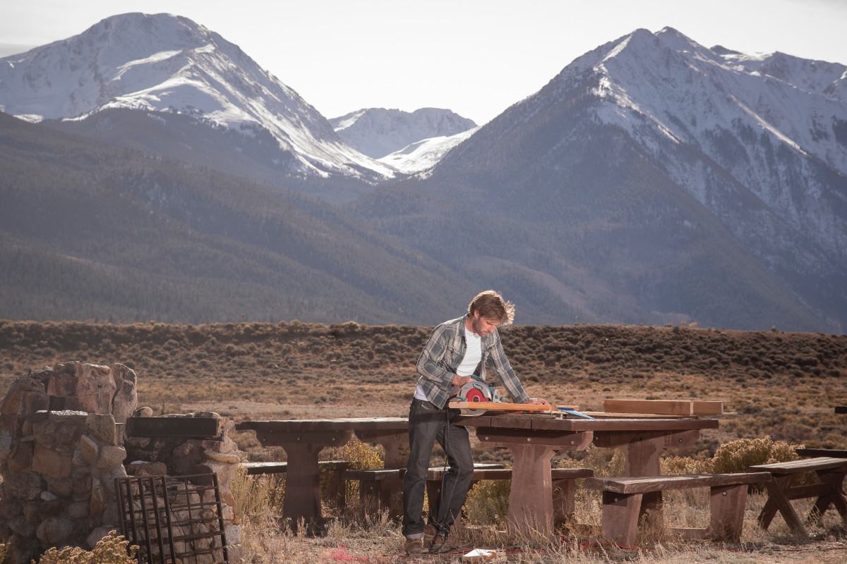 man wearing gray dress shirt standing beside table near brown mountain during daytime