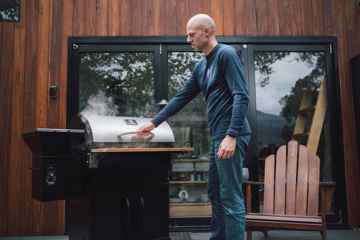 Smoke escaping from a pellet smoker as the subject opens the grill lid